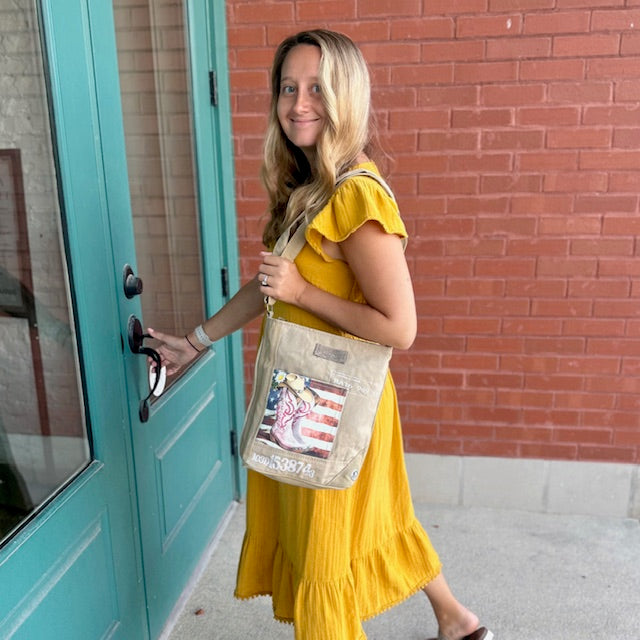 lightweight sustainable crossbody bag with pink cowgirl boots in front of an American flag.