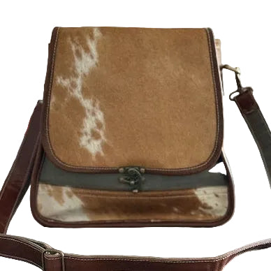 Brown cowhide pattern and Recycled Military Canvas Bag on table with a bookshelf and flowers in the background