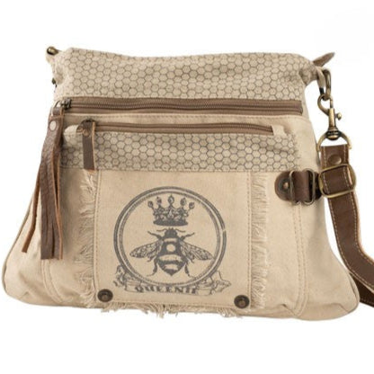 an off-white crossbody bag with the image of a bee with a crown for the full queen bee effect. Multiple zip compartments for organization.