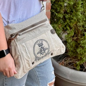 an off-white crossbody bag with the image of a bee with a crown for the full queen bee effect. Multiple zip compartments for organization.