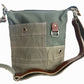A recycled military canvas crossbody bag in muted green with a brown leather strap and metal hardware.