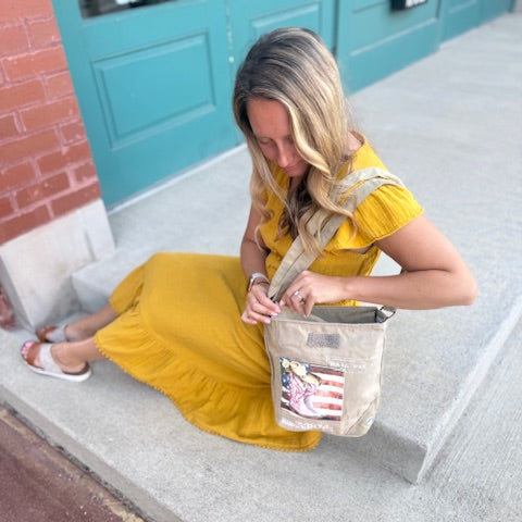 American Cowgirl Crossbody being worn by a woman. Bag has pink cowboy boots sitting in front of an American Flag .