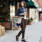 Woman walking on a sidewalk holding a coffee cup and a repurposed military bag made of upcycled military canvas with an image of a black raven sitting on a stack of books. Text on front of bag reads Black Raven Coffee Shop