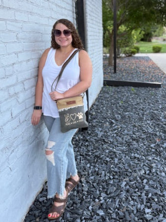our peace love dogs custom print green and tan crossbody with fringe worn as a shoulder bag.