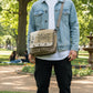 Man standing in a park wearing a recycled military canvas messenger bag with Music Festival printed on it in a vintage vibe