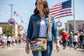 Brown recycled military canvas crossbody  bag with the Statue of Liberty design with a slip pocket on the front holding a smartphone inside.