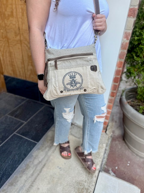 an off-white crossbody bag with the image of a bee with a crown for the full queen bee effect. Multiple zip compartments for organization.