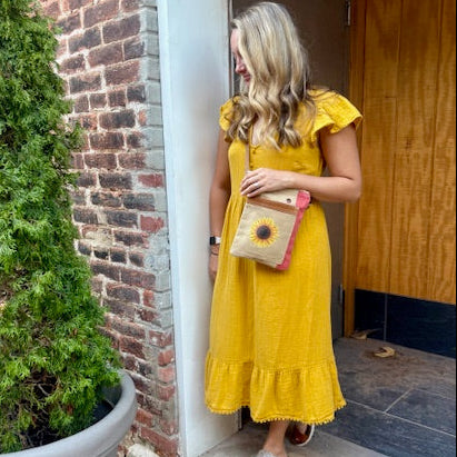 Woman in a yellow dress wearing a small passport bag  made from recycled military canvas that's tan with a salmon color side panel and a sunflower on the front.