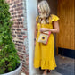 Woman in a yellow dress wearing a small passport bag  made from recycled military canvas that's tan with a salmon color side panel and a sunflower on the front.