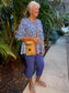 Woman in a blue floral top and pants wearing a tan recycled military canvas passport bag with a sunflower on the front