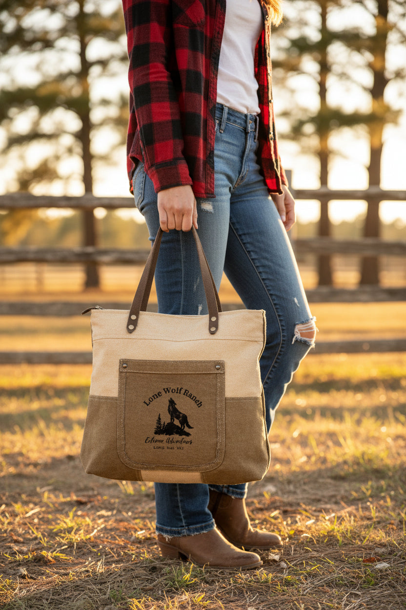 Recycled Military Canvas Tote or Shoulder Bag with brown leather accents and 'Lone Wolf Ranch Extreme Adventures print being held by a woman in a rustic outdoor setting.