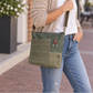 A recycled military canvas crossbody bag in muted green with a brown leather strap and metal hardware being worn.