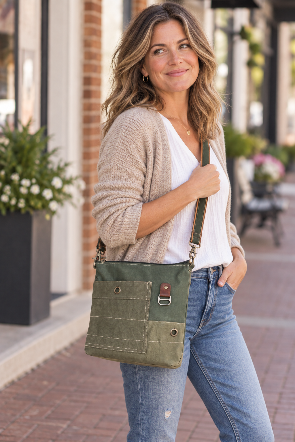 woman wearing A recycled military canvas crossbody bag in muted green with a brown leather strap and metal hardware.