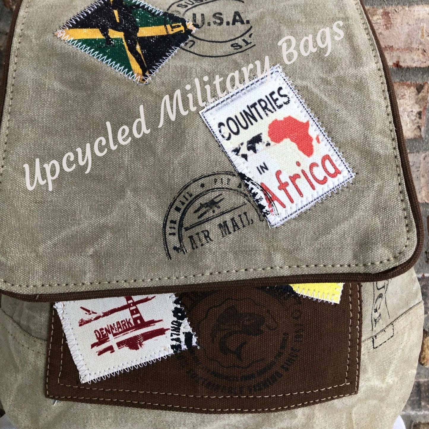 The UpCycled Travel Stamp Backpack is upcycled, crafted from re-purposed military tents, tarps and canvas. Vintage inspired with patches of travel stamps: USA, Africa, Denmark and more. Sturdy heavy canvas on this medium sized backpack. Tan with brown accents. Features include: FRONT MAGNETIC CLOSURE, ZIP TOP CLOSURE, Dimensions are 13" x 13.5" X 4", FRONT POCKET, BACK ZIPPED POCKET FULLY LINED, 1 ZIPPED INSIDE POCKET, ADJUSTABLE STRAP.