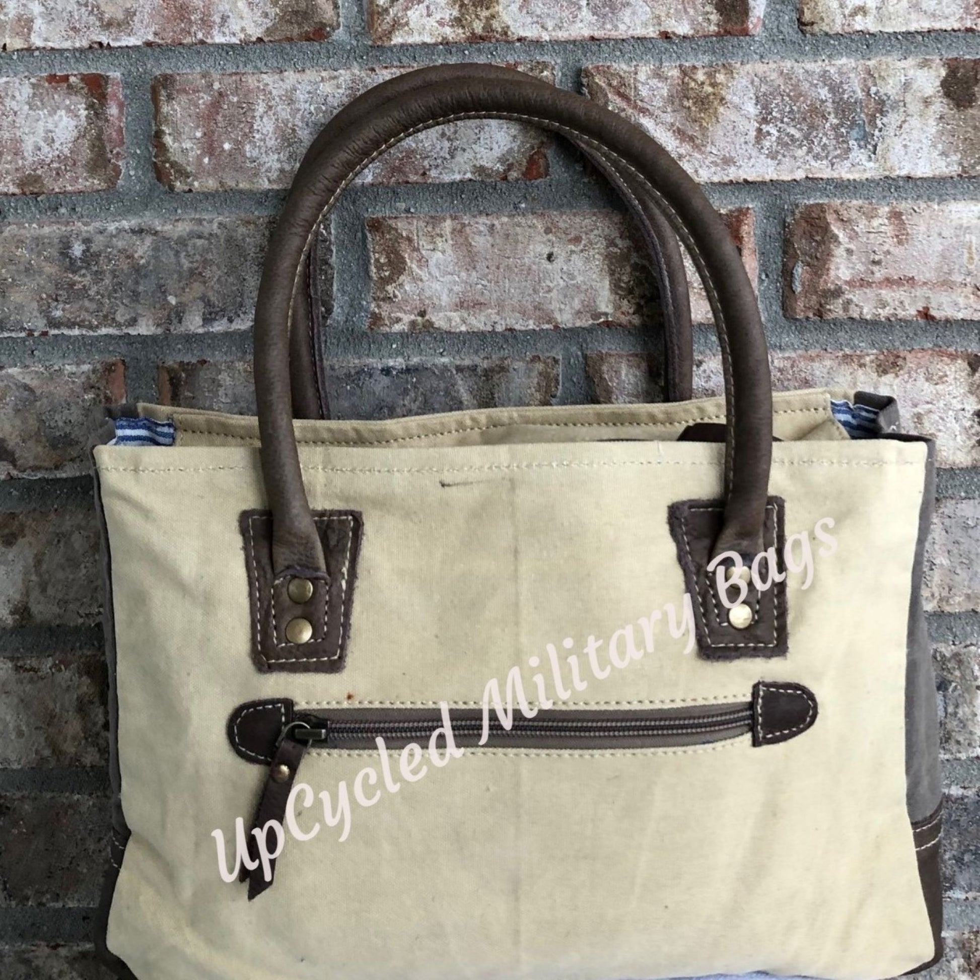 The UpCycled Vintage Buck Shoulder Bag / Tote is made from repurposed military tent and tarp canvas!  This purse gives off a vintage vibe with the Original Vintage Buck on the front.  It provides comfort with padded handles.  It has a zippered back pocket, a zipped inside pocket and is fully lined.