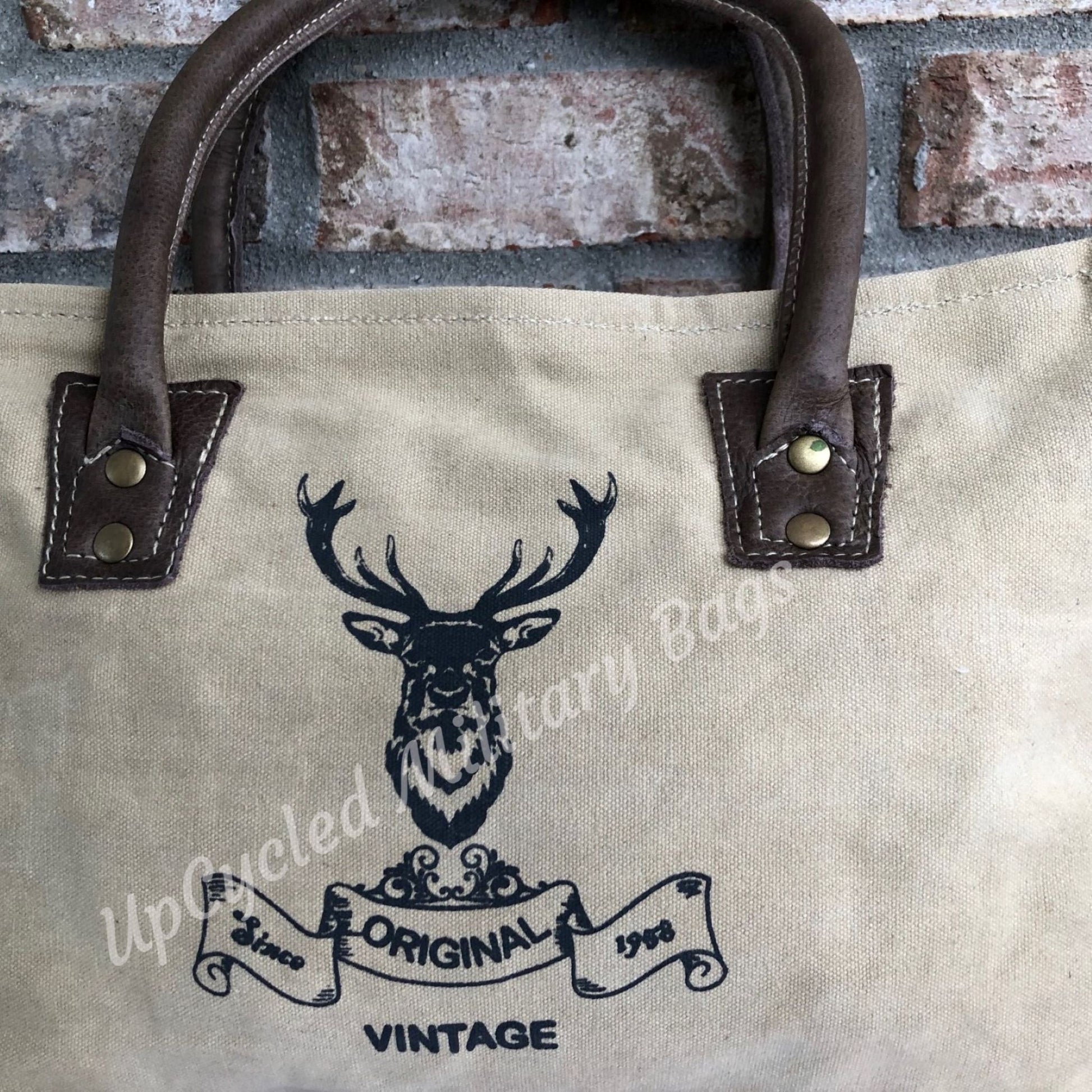 The UpCycled Vintage Buck Shoulder Bag / Tote is made from repurposed military tent and tarp canvas!  This purse gives off a vintage vibe with the Original Vintage Buck on the front.  It provides comfort with padded handles.  It has a zippered back pocket, a zipped inside pocket and is fully lined.