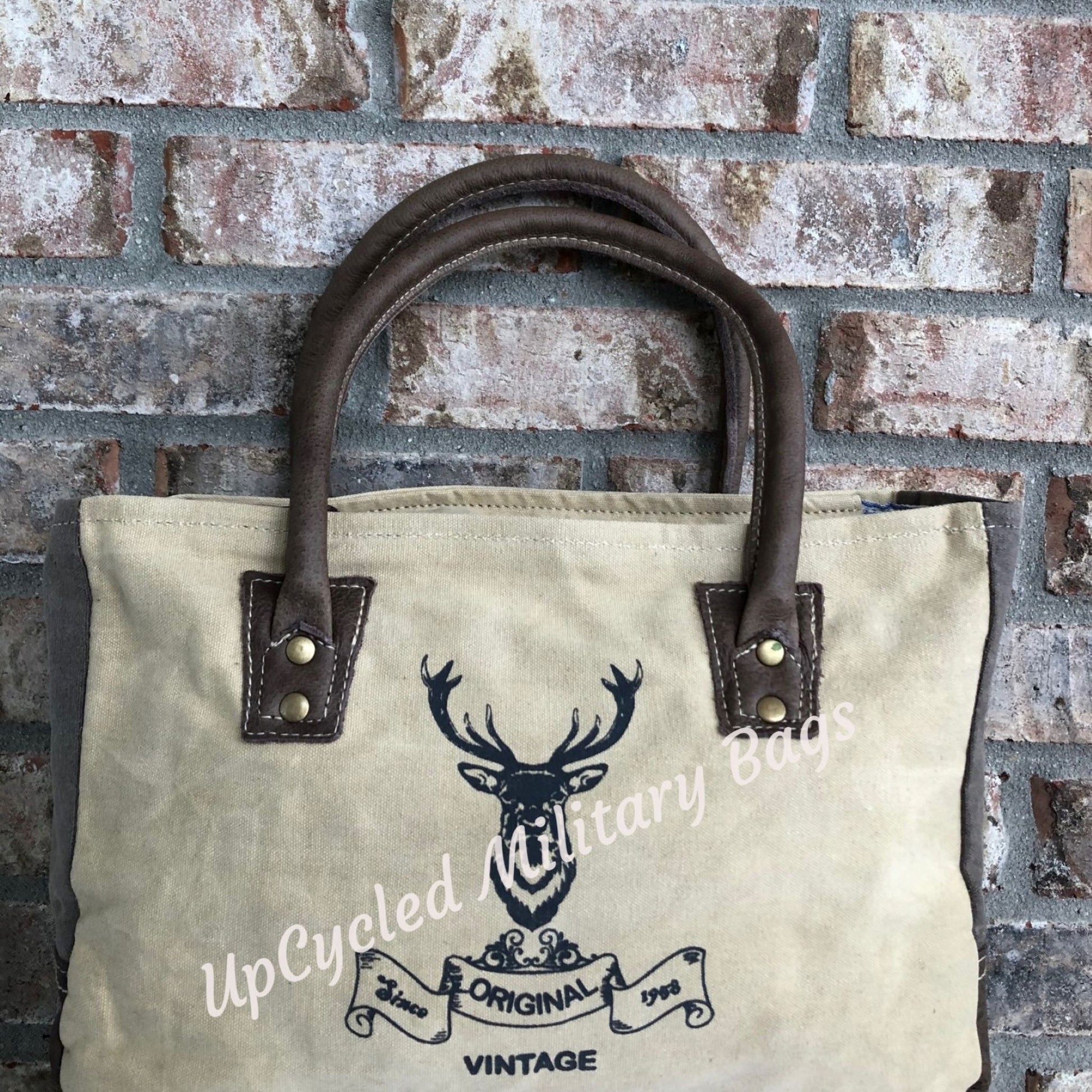 The UpCycled Vintage Buck Shoulder Bag / Tote is made from repurposed military tent and tarp canvas!  This purse gives off a vintage vibe with the Original Vintage Buck on the front.  It provides comfort with padded handles.  It has a zippered back pocket, a zipped inside pocket and is fully lined.