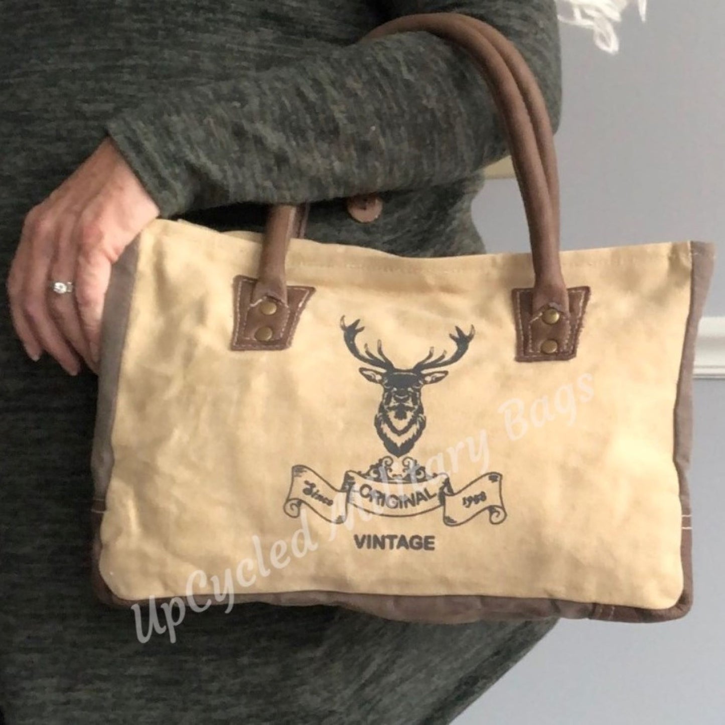 The UpCycled Vintage Buck Shoulder Bag / Tote is made from repurposed military tent and tarp canvas!  This purse gives off a vintage vibe with the Original Vintage Buck on the front.  It provides comfort with padded handles.  It has a zippered back pocket, a zipped inside pocket and is fully lined.